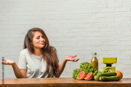 Concept of diet. Portrait of a healthy young latin woman doubting and shrugging shoulders, concept of indecision and insecurity, uncertain about something