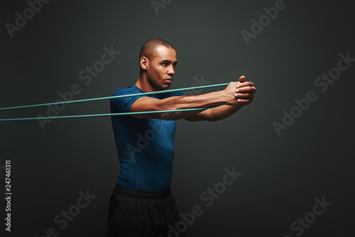Get stronger every day. Sportsman working out with resistance band over dark background