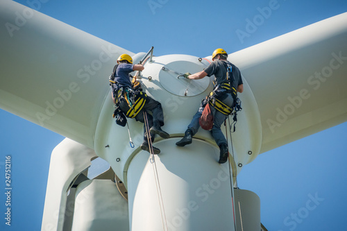 Inspection engineers preparing to rappel down a rotor blade of a wind turbine in a North German wind farm on a clear day with blue sky.