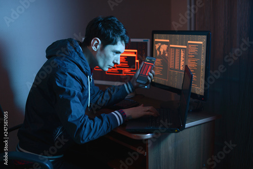 Male hacker holding the phone in his hands trying to hack the mobile device cloud in the dark under neon light