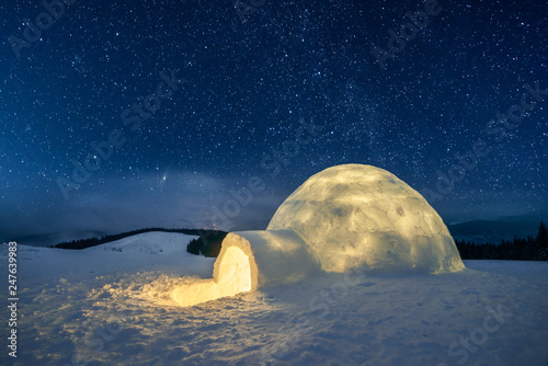 Fantastic winter landscape glowing by star light. Wintry scene with snowy igloo and milky way in night sky