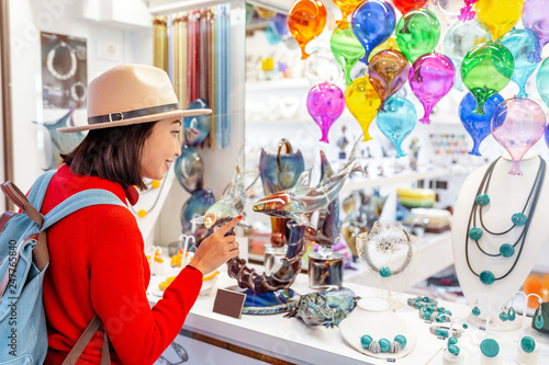 Woman tourist shopping for colorful decorated objects made of a famous murano glass in a shop window in Venice