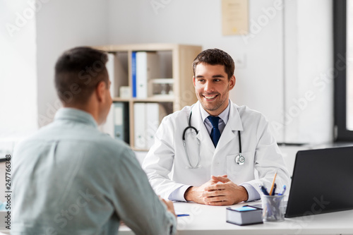 medicine, healthcare and people concept - smiling doctor talking to male patient at medical office in hospital