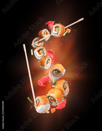Fresh sushi rolls with ginger frozen in the air on black background