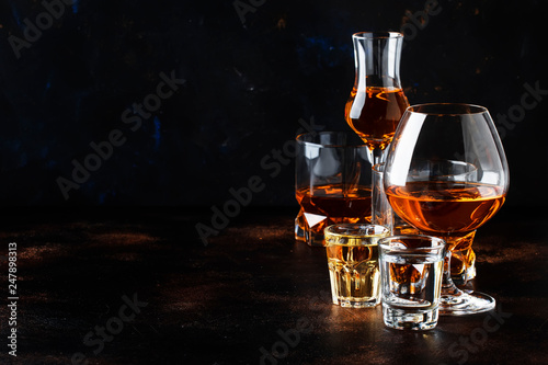 Selection of hard alcoholic drinks in big glasses and small shot glass in assortent: vodka, rum, cognac, tequila, brandy and whiskey. Dark vintage background, selective focus, copy space