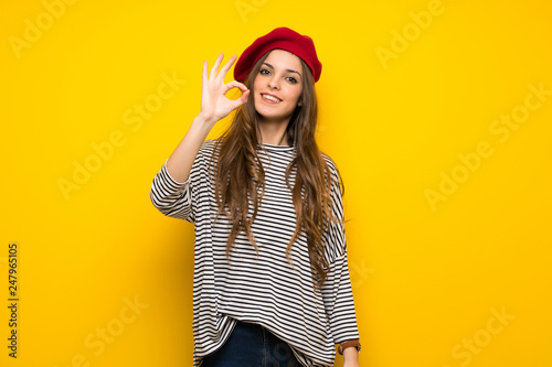 Girl with french style over yellow wall showing an ok sign with fingers