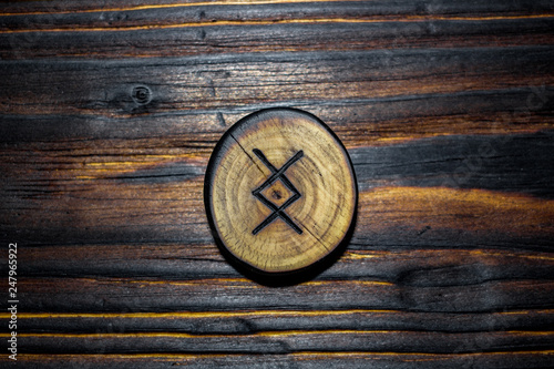 Rune Ingwaz (Yngvi) carved from wood on a wooden background - Elder Futhark