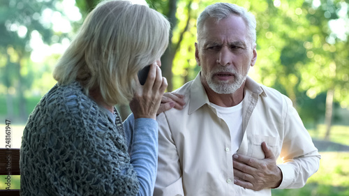 Old couple sitting on bench, man suffering arrhythmia, wife calling emergency