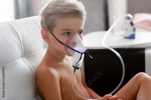 Young boy using nebulizer for asthma and respiratory diseases at home. Teenager doing inhalation inhales couples containing medication. Concept of home treatment. Medical procedures.
