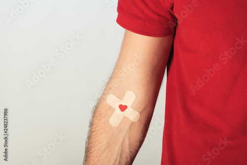 Partial view of patient in red t-shirt with plasters on grey background, blood donation concept