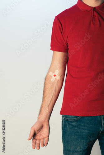 Partial view of patient in red t-shirt with plasters, blood donation concept