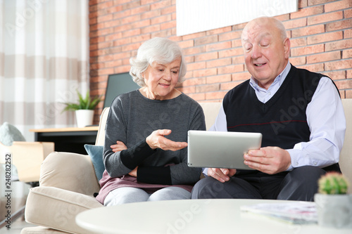 Elderly couple using tablet PC on sofa in living room