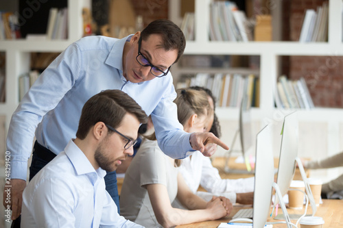 Angry boss criticizing scolding sad male employee for computer mistake