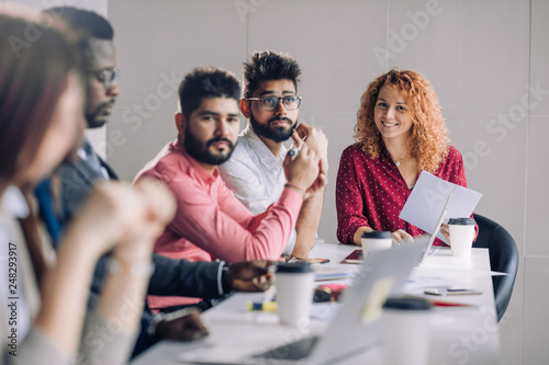 Mixed race diverse group of people in formal wear, sitting in raw at office table attending annual refresher course, led by a red-haired female coach