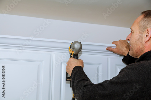 Handyman using brad nail gun on installation crown moulding wall cabinets framing trim