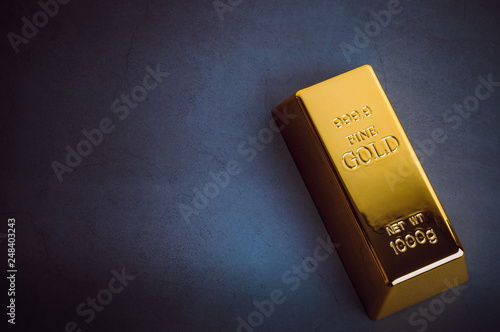 An ingot of gold metal bullion of pure brilliant diagonally located on a blue textured background.