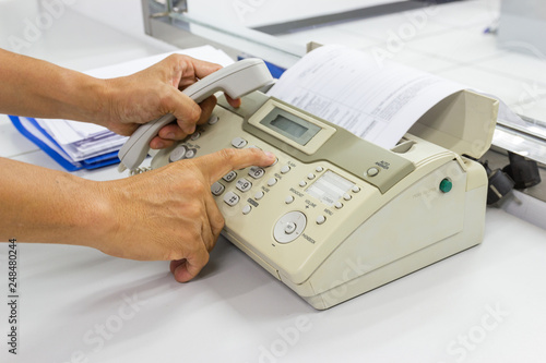 Hand man are using a fax machine send paper in the office Business concept 