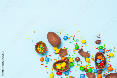 Broken and whole chocolate Easter eggs, multicolored sweets on blue background. Concept of celebrating Easter, Easter decorations, search for sweets for Easter Bunny. Flat lay, top view. Copy Space
