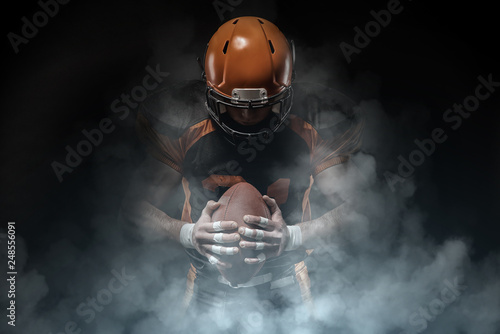 American football player on a dark background in smoke in black and orange equipment.