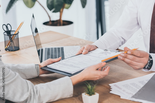 cropped view of businessman giving compensation claim form to woman at workplace