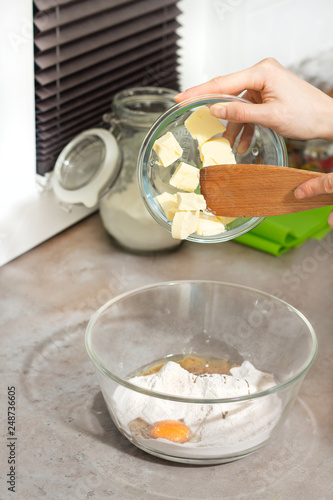 Przygotowanie składników do wypieków. Kobiece dłonie dodają masło do miski z mąką i jajkami Dodawanie margaryny do mąki i jajek.
