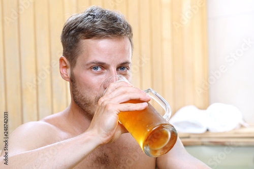 Picie piwa. Przystojny mężczyzna zażywa kąpieli w bali z woda termalną pijąc piwo kuflowe.