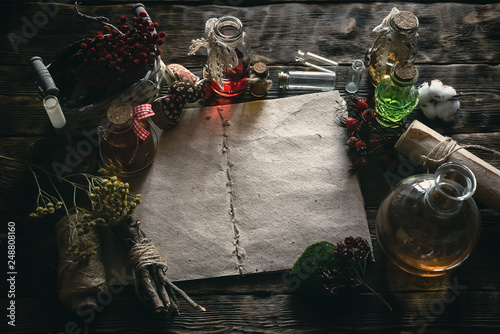 Ancient recipe scroll book and various dry herbs on a table of witch doctor. Herbal medicine essential oil on a table. Witchcraft background with copy space.