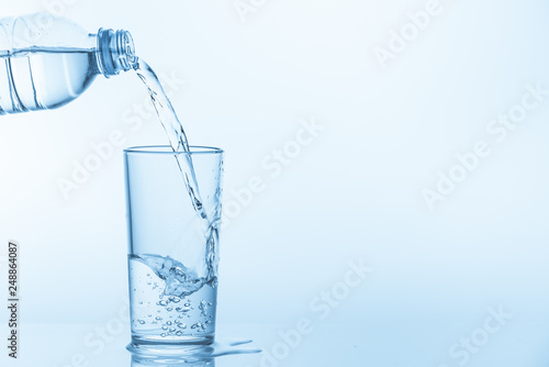 Pouring water from bottle into glass on blue background. Photo with copy space.
