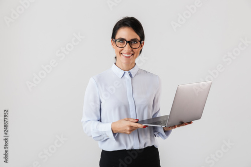 Portrait of young businesswoman wearing eyeglasses holding silver laptop in the office, isolated over white background