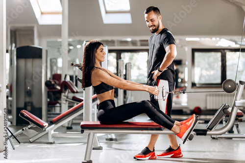 Pretty slim girl is doing exercises for the abdominals on a special exercise machine under the supervision of a coach in the gym