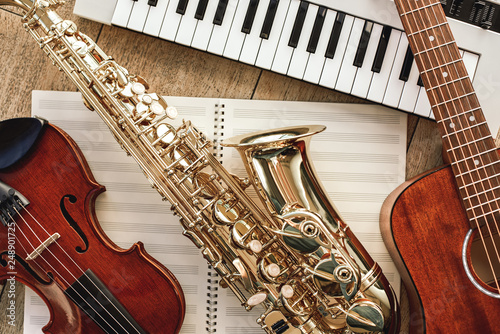 Power of music. Top view of musical instruments set: synthesizer, guitar, saxophone and violin lying on the sheets for music notes over wooden floor