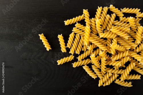 farfalle Raw Fusilli italian pasta on a wood black textured background. Close-up view from the top. Free space for text.