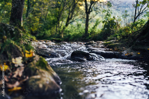 A river creek with a small waterfall. Sunset and strong detail bokeh view. blue calm warm water