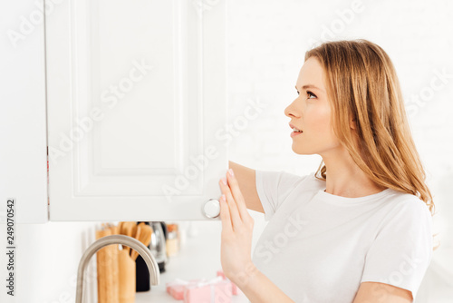beautiful girl in pajamas opening cupboard in kitchen with copy space