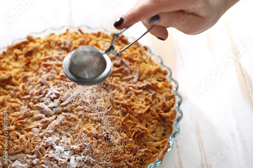 Tarta z jabłkami. Kobieta obsypuje ciasto cukrem pudrem.