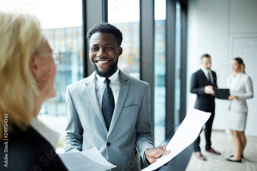 Young smiling African-american businessman in formalwear showing new contract to his colleague in conference hall