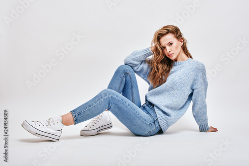 What do you mean? Brown-haired, cute girl sitting on the floor, touching her hair with a surprised look, isolated over white background