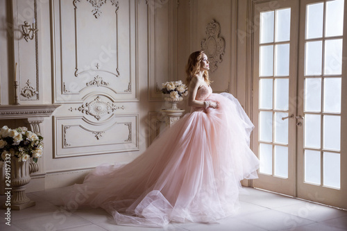 Beautiful young blond woman in luxurious long pink dress posing in vintage room interior. indoor studio shot.