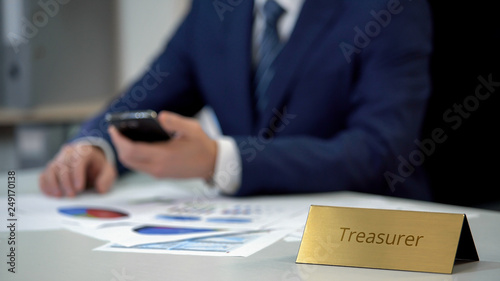 Male treasurer working with documents, calculating company budget on smartphone