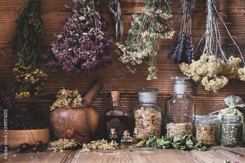 Dried herbs hanging over bottles of tinctures and oils