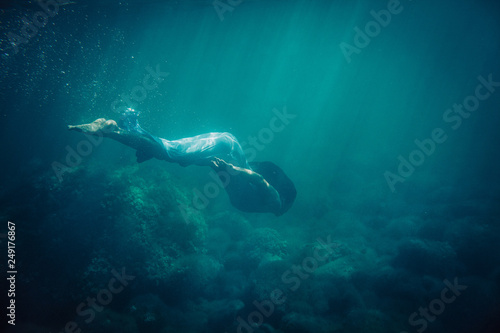 brunette girl in long blue dress dives underwater in the sea