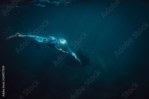 brunette girl in long blue dress swimming underwater