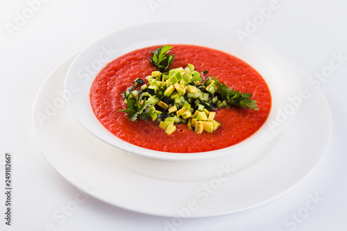 Spanish soup gazpacho with avocado and cucumber on a white plate on a light background (close)