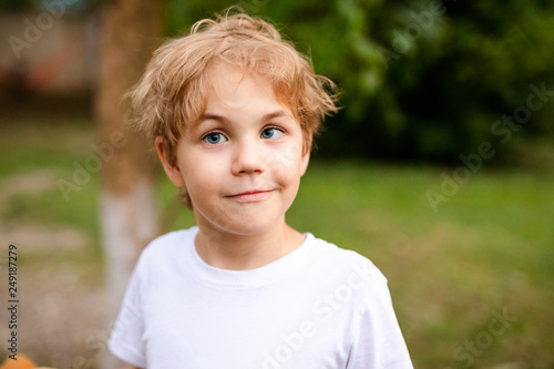 Blonde smiling boy with strabismus in warm park