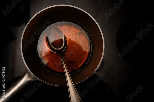 pot and spoon with beef stock while cooking a red wine morel sauce on a black stove, dark background with copy space, high angle view from above