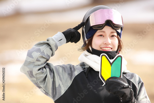 初心者マークを持ちヘルメットを指さすスノーボードウェアの女性