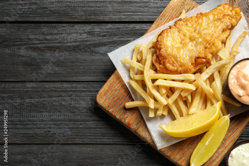 Board with British traditional fish and potato chips on wooden background, top view. Space for text