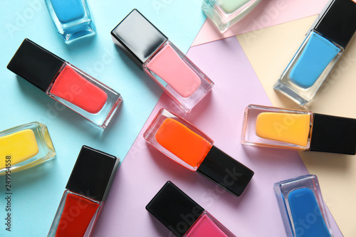 Bottles of nail polish on color background, top view