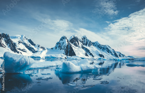 Blue Ice covered mountains in south polar ocean. Winter Antarctic landscape. The mount's reflection in the crystal clear water. The cloudy sky over the massive rock glacier. Travel wild nature