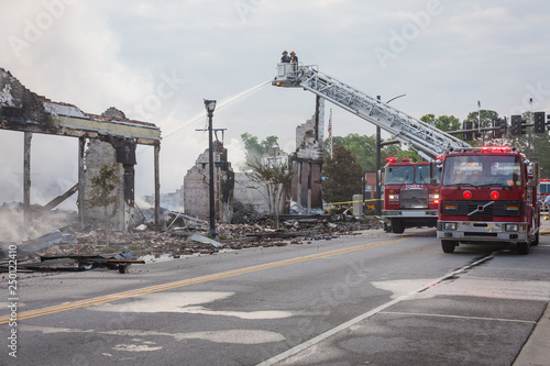 Firemen on ladder truck with water hose extinguish fire with building in ruins